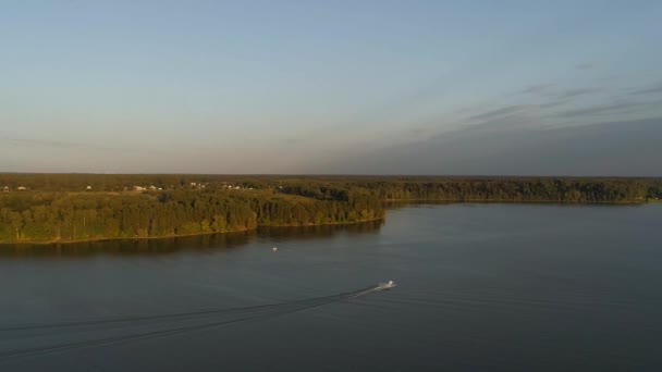 在夕阳西下的阳光下，一架无人驾驶飞机在Istra水库上拍了一枪，无人驾驶飞机飞越森林和湖面，一艘快艇沿着湖面疾驰而过。俄罗斯美丽的自然 免版税图库视频片段