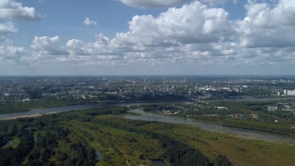 A drón magasan repül az erdő szélén, a horizonton van egy város különböző épületekkel, gyönyörű bolyhos fehér felhők lebegnek a város felett. Város madártávlatból Jogdíjmentes Stock Videó