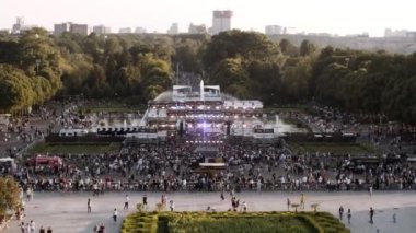 Büyük bir şehirdeki fıskiyelerin yakınındaki bir parkta gösteri için büyük bir sahne. Hafif müzikli popüler bir grubun sahnesinde seyirciler açık hava konserine geldi.