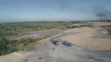 İnsansız hava aracı, güçlü damperli kamyonların zorlu off-road alanlarını kolayca aştığı toprak bir yola doğru uçuyor. Madencilik. Gezegenin endüstriyel ölçekte yok edilmesi. Doğa kirliliği