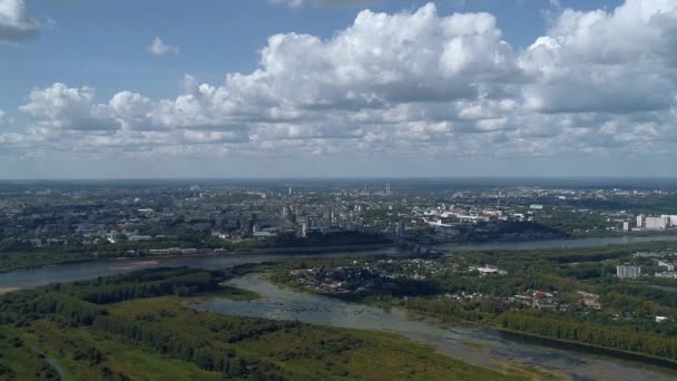 Беспилотник летит высоко над окраиной зеленого города на берегу реки, над городом плавают красивые пушистые белые облака. Красивый город с высоты птичьего полета — стоковое видео