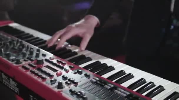 Musician keyboard player in a popular band. Close-up of the pianists hands on stage, who plays the synthesizer along with his band. Performances by a musical group at a concert in a nightclub — Stock Video