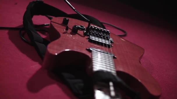 Närbild av en röd elgitarr ligger på ett rött golv. Populär musik med elgitarr i konsert. Gitarren är stämd och redo för en rockbandsföreställning. Musikinstrument ur fokus — Stockvideo