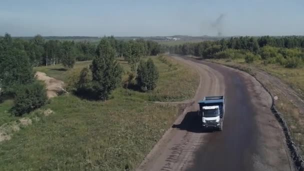 El dron vuela hasta un camino de tierra a lo largo del cual un camión volquete pesado está conduciendo en un chasis de cinco ejes. El camión de basura se va a cargar. Minería. La destrucción del planeta a escala industrial — Vídeo de stock
