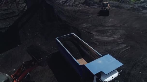 A drón egy nehéz teherautóval repked, amibe a rakodó szenet tölt. Szénérccel rakodó teherautók, ipari méretű bányászat. nyitott bánya szénbánya. — Stock videók