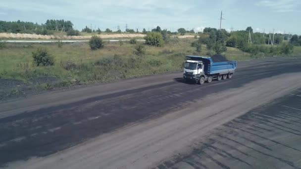 El dron sigue un camión volquete pesado en un chasis de cinco ejes. El camión de basura está cargado con carbón. Minería. La destrucción del planeta a escala industrial. contaminación de la naturaleza — Vídeos de Stock