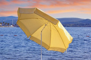 Güneş batarken körfez kıyısında sarı plaj şemsiyesi. Karadağ