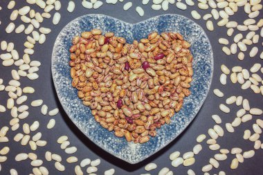 Kalp şeklinde kahve çekirdekleri ve siyah masada beyaz fasulyeler.