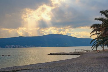 Bulutlu sonbahar günbatımı. Gün ışığı bulutların arasından parlar. Güzel Akdeniz manzarası. Karadağ, Adriyatik Denizi. Tivat şehri yakınlarındaki Kotor Körfezi kıyısında.