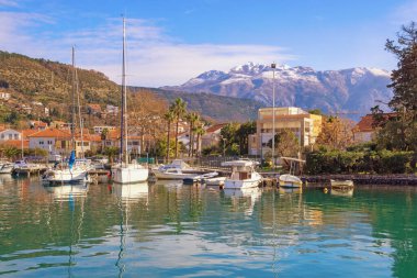 Güzel bir kış Akdeniz manzarası. Limandaki yeşil kasaba ve tekneler karlı dağlara karşı. Karadağ, Kotor Körfezi. Tivat şehri, Kalimanj marinası manzaralı.