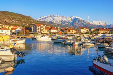 Güneşli kış gününde güzel Akdeniz manzarası. Limanda balıkçı tekneleri ve karlı dağlarda. Karadağ, Kotor Körfezi. Tivat şehri, Kalimanj marinası manzarası ve Lovcen dağları