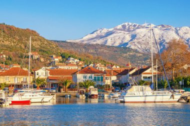 Güneşli kış günü, güzel Akdeniz manzarası. Limandaki yeşil kasaba ve balıkçı tekneleri karlı dağlara karşı. Karadağ, Kotor Körfezi. Tivat şehri, Kalimanj marinası manzarası ve Lovcen dağları