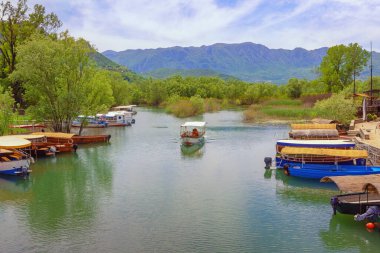  Karadağ. Ulusal Park Gölü Skadar, Virpazar köyü. Nehirde turist tekneleri olan güzel dağ manzarası