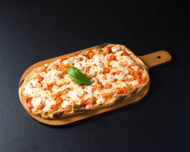 Domatesli Pinsa, mozzarella ve fesleğenli, koyu taşlı arka planda kesim tahtası.