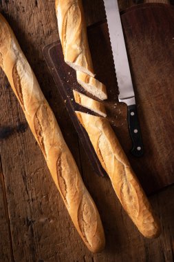Tahta masada bıçaklı baget. İkiye bölünmüş baget. Bir dilim ekmek. Tipik Fransız ekmeği