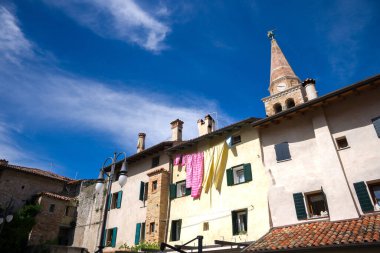 Grado, İtalya. 15 Mayıs 2021, tipik İtalyan evleri. Eski Grado kasabasının pencerelerinde kuruyacak giysileri var. Arka planda bazilikanın çan kulesi var.