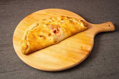 Pizza calzone . Kapalı pizza hamuru, doldurulmuş ve pişirilmiş. Ahşap kesim tahtasının üzerinde.