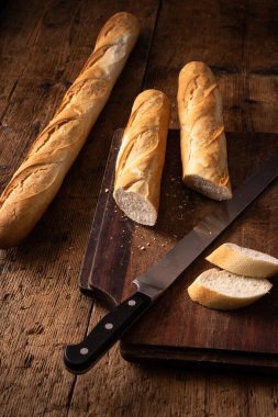 Tahta masada bıçaklı baget. İkiye bölünmüş baget. Bir dilim ekmek. Tipik Fransız ekmeği