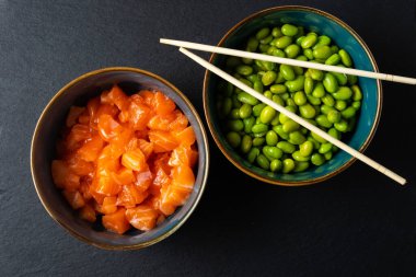 Bir kase çiğ ton balığı ve üzerinde yemek çubukları olan edamame. Karanlık arka plan. Tipik Asya malzemeleri