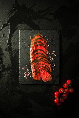 Siyah taşın üzerinde otlarla tütsülenmiş somon balığı ve Pachino domatesleri. tepeden görünüm