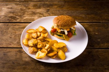 Tahta masanın üzerinde hamburger ve patates kızartması tabağı.