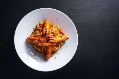 Koyu arkaplanda karidesli Busara spagettisi tabağı.