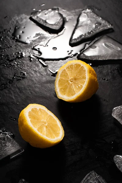 lemon cut on black background with pieces of ice