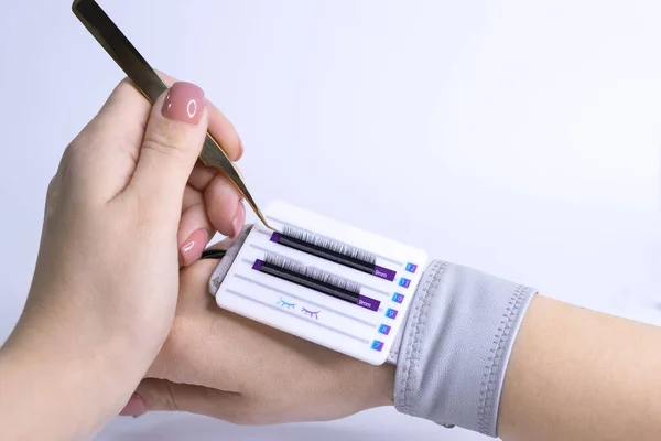 Female hand holds eyelash extension tweezers and takes eyelashes — Stock Photo, Image