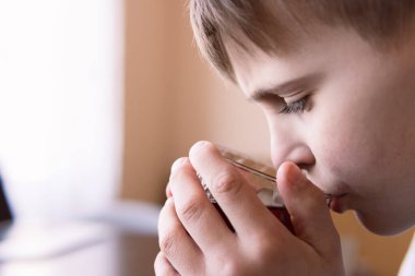 Avrupalı görünümlü ve sarı saçlı bir çocuk fincandan çay içer.