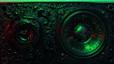 Musical speaker in water drops with beautiful colored backlight multicolored wet Musical speaker close-up. Lighting to the beat of the music. High quality FullHD footage