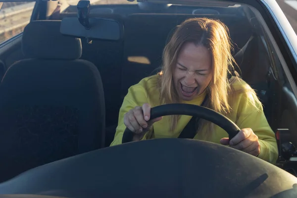 a girl of European appearance sits behind the wheel of a car sad, holds on to the steering wheel and screams strongly does not know what to do the car broke down on the road High quality photo