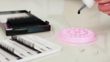 eyelash extension materials close-up. Glue is dripped on a pebble Pink colour for glue, slow motion, eyelash extensions and tweezers lie nearby. High quality FullHD footage