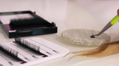 Close-up. The master takes a bunch of curved artificial eyelashes with tweezers from the tablet and dips it in glue. The process of eyelash extensions in a beauty salon. slow motion. High quality 4k 