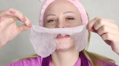smiling girl with a pink bandage on her head makes a cloth face mask. A girl of European appearance with a tattoo on her left arm. The concept of a well-groomed and young face. High quality 4k footage