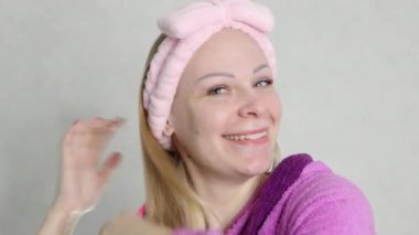  girl with blond hair, close-up of her face,wearing a pink bandage on her head, standing in pink dressing gown combing her hair with a pink comb looks directly into the camera. High quality 4k footage