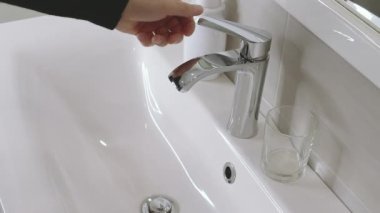 a mans hand isolated on a light background turns on the water in a white washbasin, a man in the bathroom, slow motion, shooting angle from above, slow motion. High quality FullHD footage