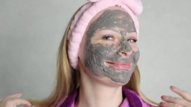 smiling girl with blond hair on her head with a pink bandage, looking at the camera smiling, on her face a gray bubble mask. behind a light background close-up of the face. High quality 4k footage