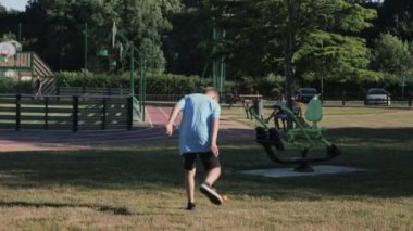 a boy of European appearance in dark shorts and a blue T-shirt plays in the park on the playground on the green grass with a ping pong ball. High quality 4k footage