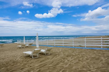 Turkuaz körfez, kumlu sahil, yeşil dağlar ve bitkiler, mavi gökyüzü, beyaz bulutlar arka plan, Capo Vaticano kaya platformu, Calabria, güney İtalya.