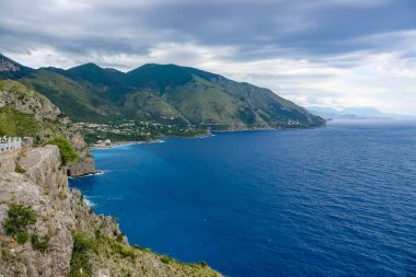 Turkuaz körfez, kumlu sahil, yeşil dağlar ve bitkiler, mavi gökyüzü, beyaz bulutlar arka plan, Capo Vaticano kaya platformu, Calabria, güney İtalya.