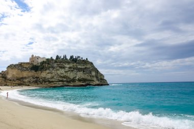 Turkuaz körfez, kumlu sahil, yeşil dağlar ve bitkiler, mavi gökyüzü, beyaz bulutlar arka plan, Capo Vaticano kaya platformu, Calabria, güney İtalya.