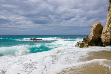 Turkuaz körfez, kumlu sahil, yeşil dağlar ve bitkiler, mavi gökyüzü, beyaz bulutlar arka plan, Capo Vaticano kaya platformu, Calabria, güney İtalya.