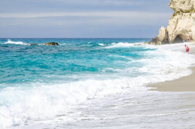 Turkuaz körfez, kumlu sahil, yeşil dağlar ve bitkiler, mavi gökyüzü, beyaz bulutlar arka plan, Capo Vaticano kaya platformu, Calabria, güney İtalya.