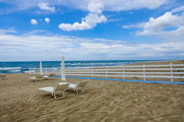 Turkuaz körfez, kumlu sahil, yeşil dağlar ve bitkiler, mavi gökyüzü, beyaz bulutlar arka plan, Capo Vaticano kaya platformu, Calabria, güney İtalya.