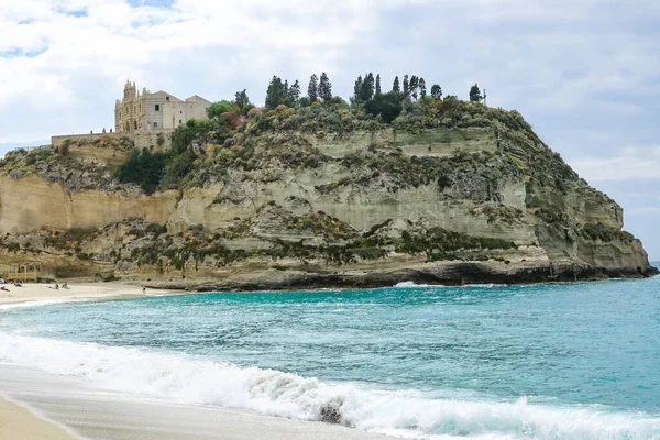 Turkuaz körfez, kumlu sahil, yeşil dağlar ve bitkiler, mavi gökyüzü, beyaz bulutlar arka plan, Capo Vaticano kaya platformu, Calabria, güney İtalya.