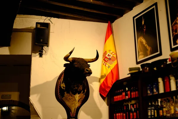 Boğa başı, şarap şişeleriyle dolu tipik bir barda İspanyol bayrağının yanında boğa güreşi kupası olarak duruyor. İspanya