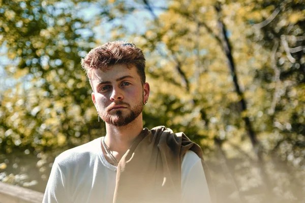 Şık ve gizemli sarışın bir adamın portresi. Güneş ışığında ağaçların arkasına gizlenmiş mavi gözlü genç bir adam.