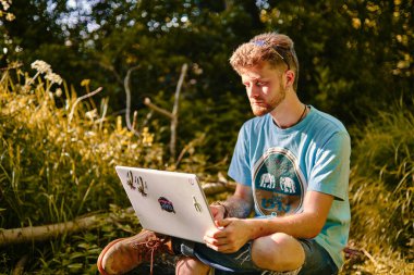 Genç girişimci dışarıda, dizüstü bilgisayarında ciddi bir yüzle çalışıyor. Sarışın, parkta dizüstü bilgisayarla ders çalışıyor.