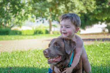 Küçük çocuk bahçede bir köpeğe sarılıyor.