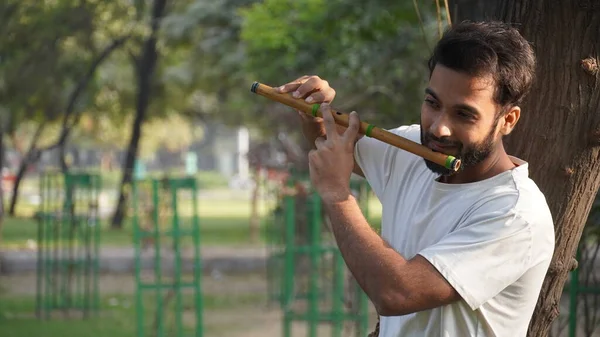Bansuri player playing music in sunshine at Park - Indian Flute Player